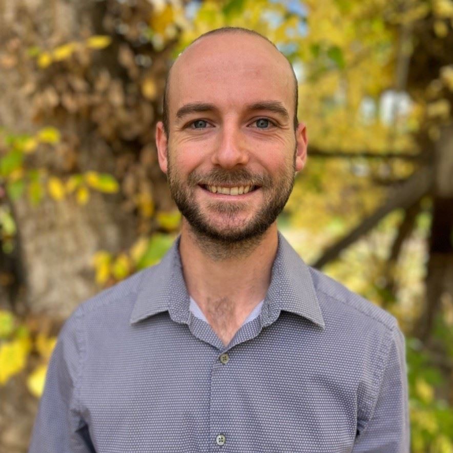 Headshot of Dylan Cox in front of green trees